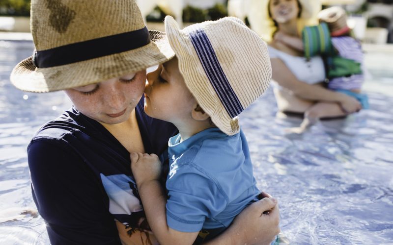 Family in outdoor swimming pool, young boy holding younger brother