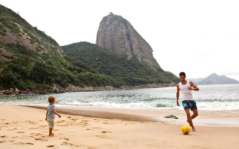 Father and son playing football on beach, Rio de Janeiro, Brazil