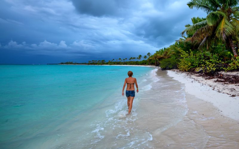 Back view teenage girl walking on a tropical beach with palm trees and ocean