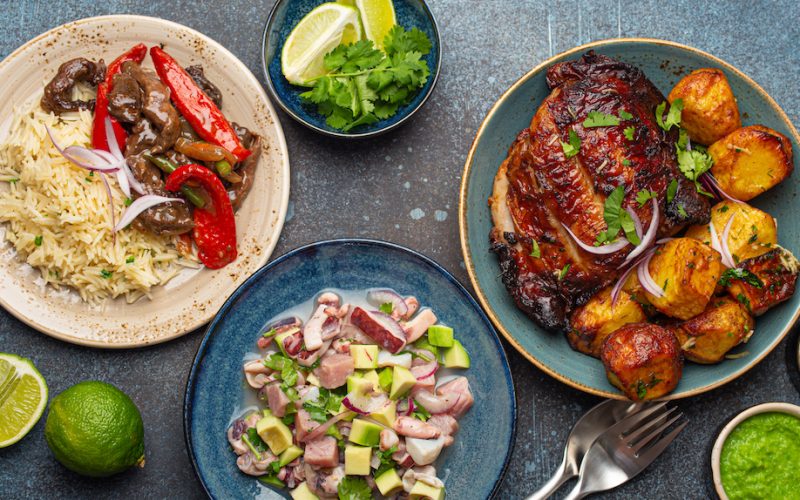 Set of assorted dishes of Peruvian cuisine: beef and peppers Lomo saltado, Peruvian ceviche with fish and seafood, roasted chicken and french fries, salsa dip on rustic stone table from above